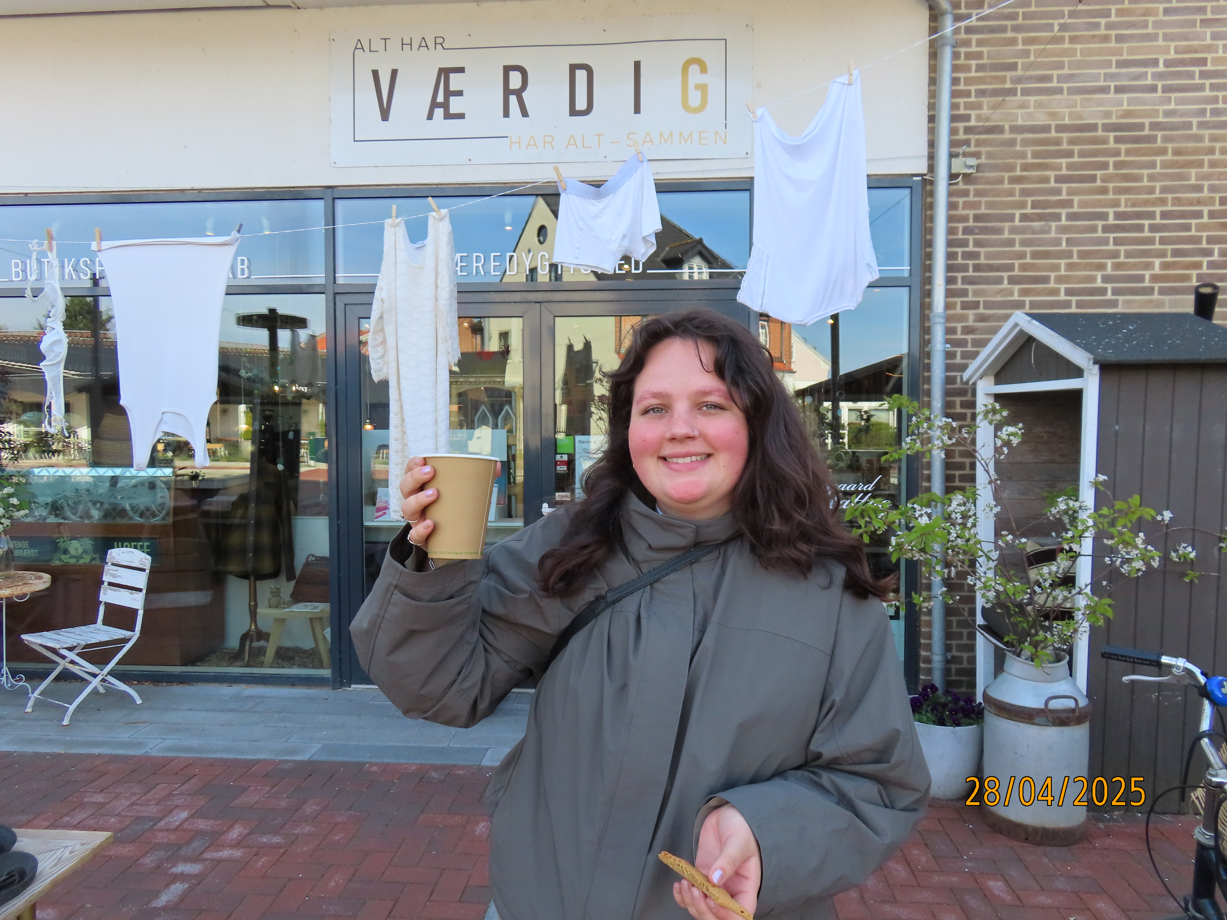 Pige foran butik værdig, med en kop kaffe.